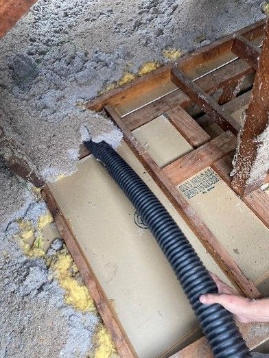 A person is using a vacuum hose to clean a hole in the floor.