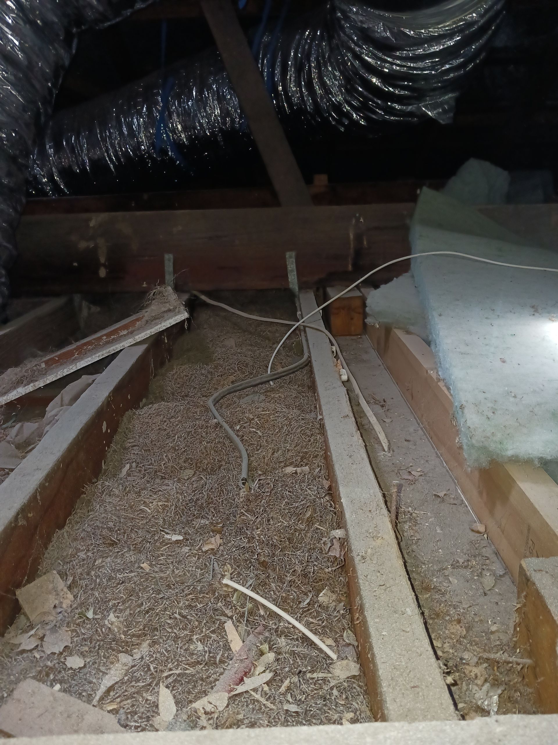 Attic interior with wood beams, insulation, and debris. Ductwork visible at the top.