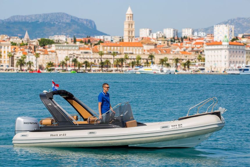 A man is driving a boat in the ocean with a city in the background.