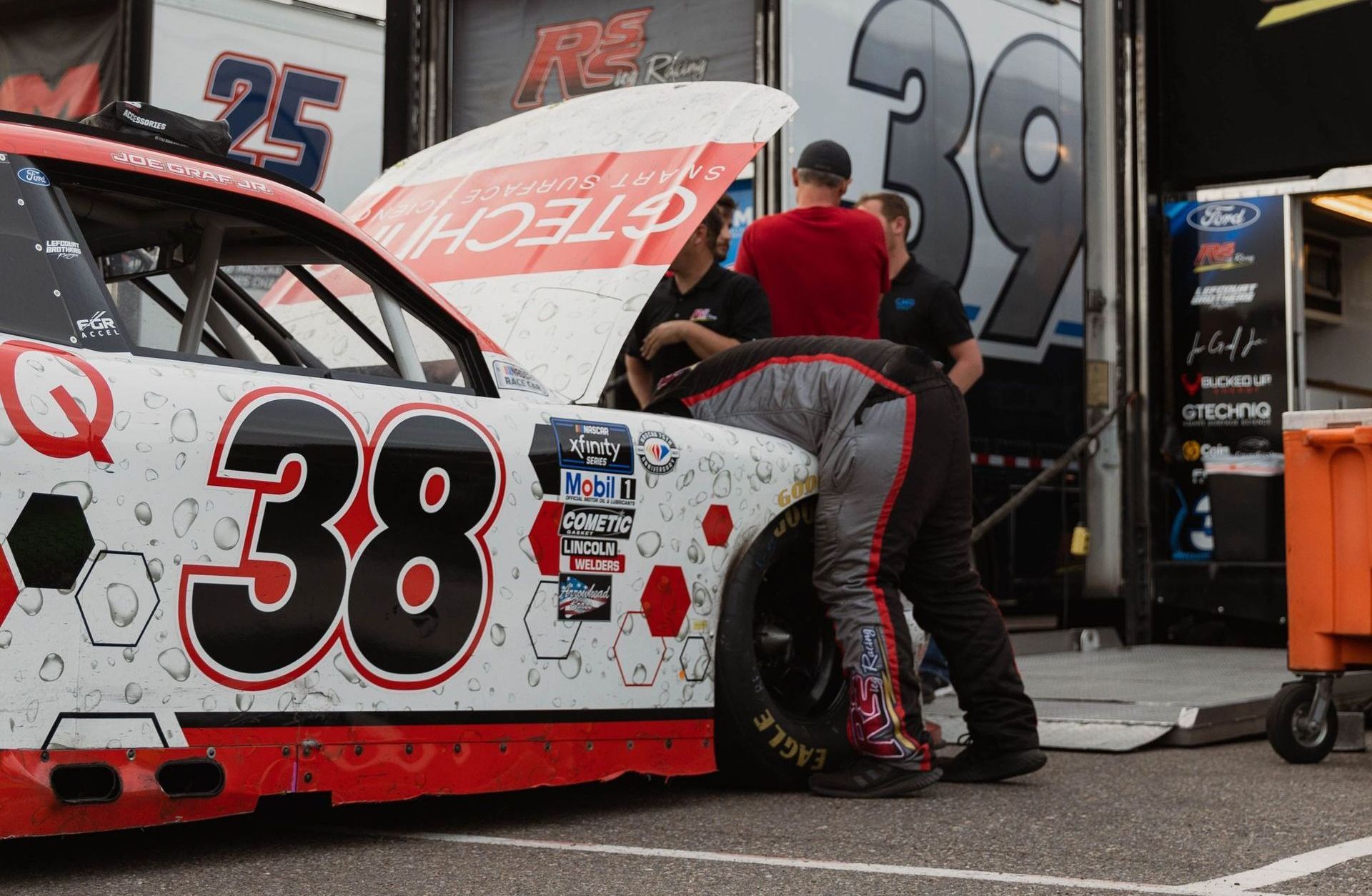 Race car, #38, being worked on by pit crew in front of a garage.