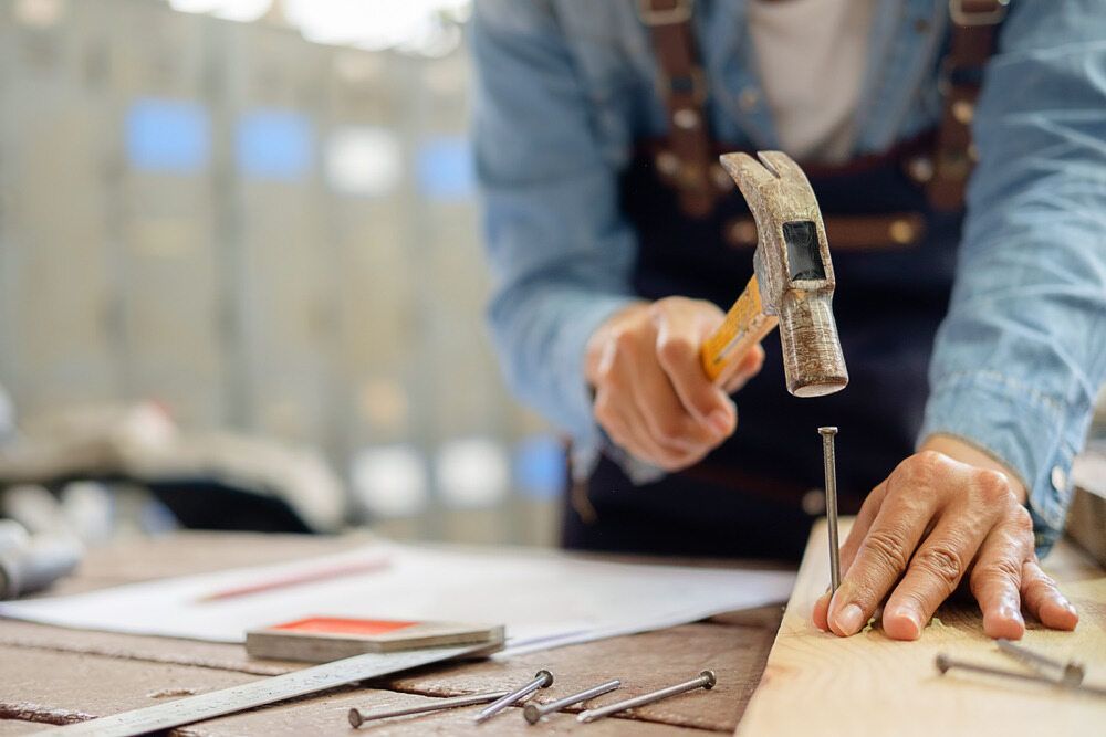 A Man Is Hammering A Nail Into A Piece Of Wood — Damn Fine Constructions In Bellingen, NSW