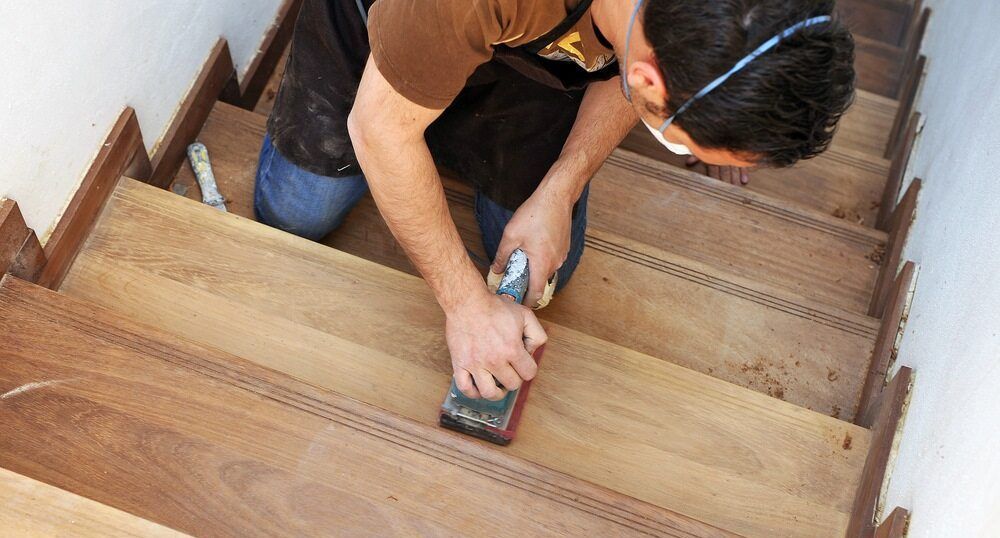A Man Is Sanding A Wooden Staircase With A Sander — Damn Fine Constructions In Bonville, NSW