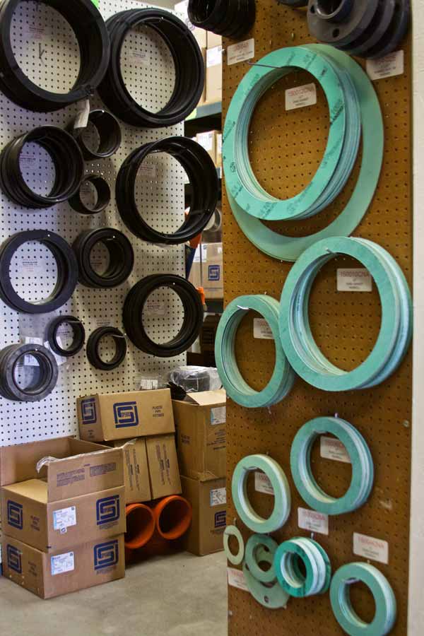 Assortment of black and teal circular gaskets on a pegboard wall in a warehouse setting, with boxes below.