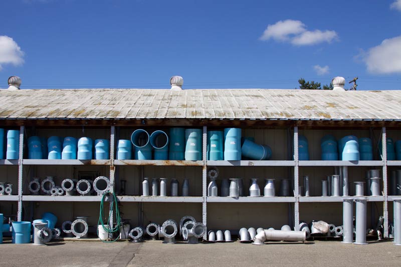 Shelves of blue and gray plumbing pipes and fittings in front of a building under a blue sky.