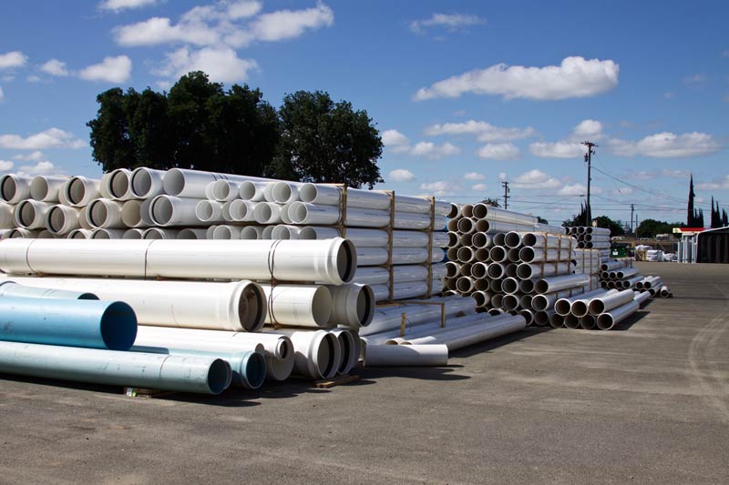 Piles of white and blue PVC pipes stacked outdoors against a blue sky.