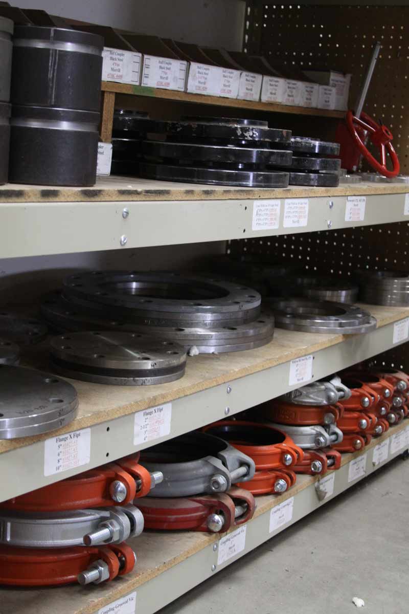Shelves stocked with industrial metal parts in a warehouse setting. Orange and black components are visible.