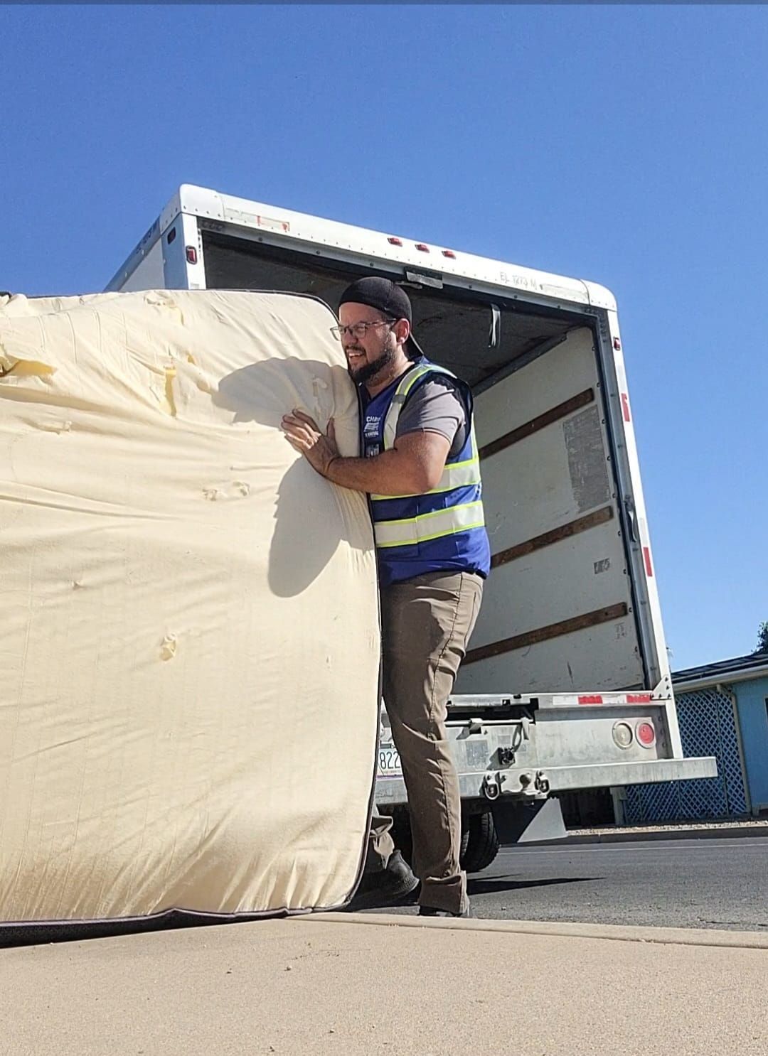 Man in vest carries large, beige, rolled-up material from a truck on a sunny day.