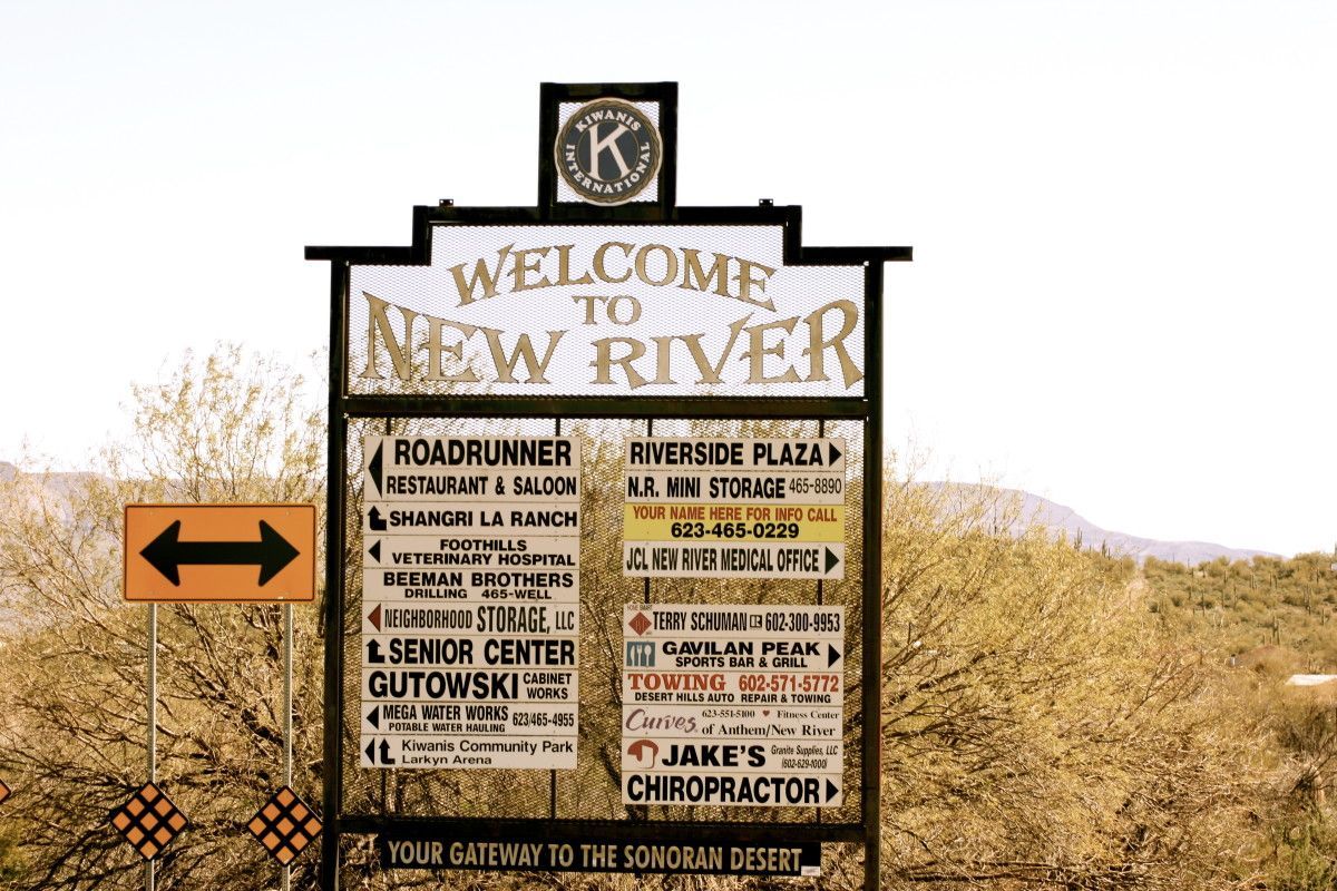 Welcome sign to New River with business listings, arrow, and mountain backdrop.