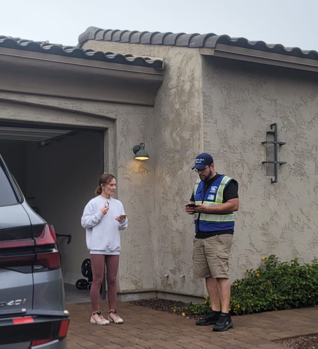 Woman and delivery person at a garage. Person looking at phone, the other holding a phone. Cloudy day.