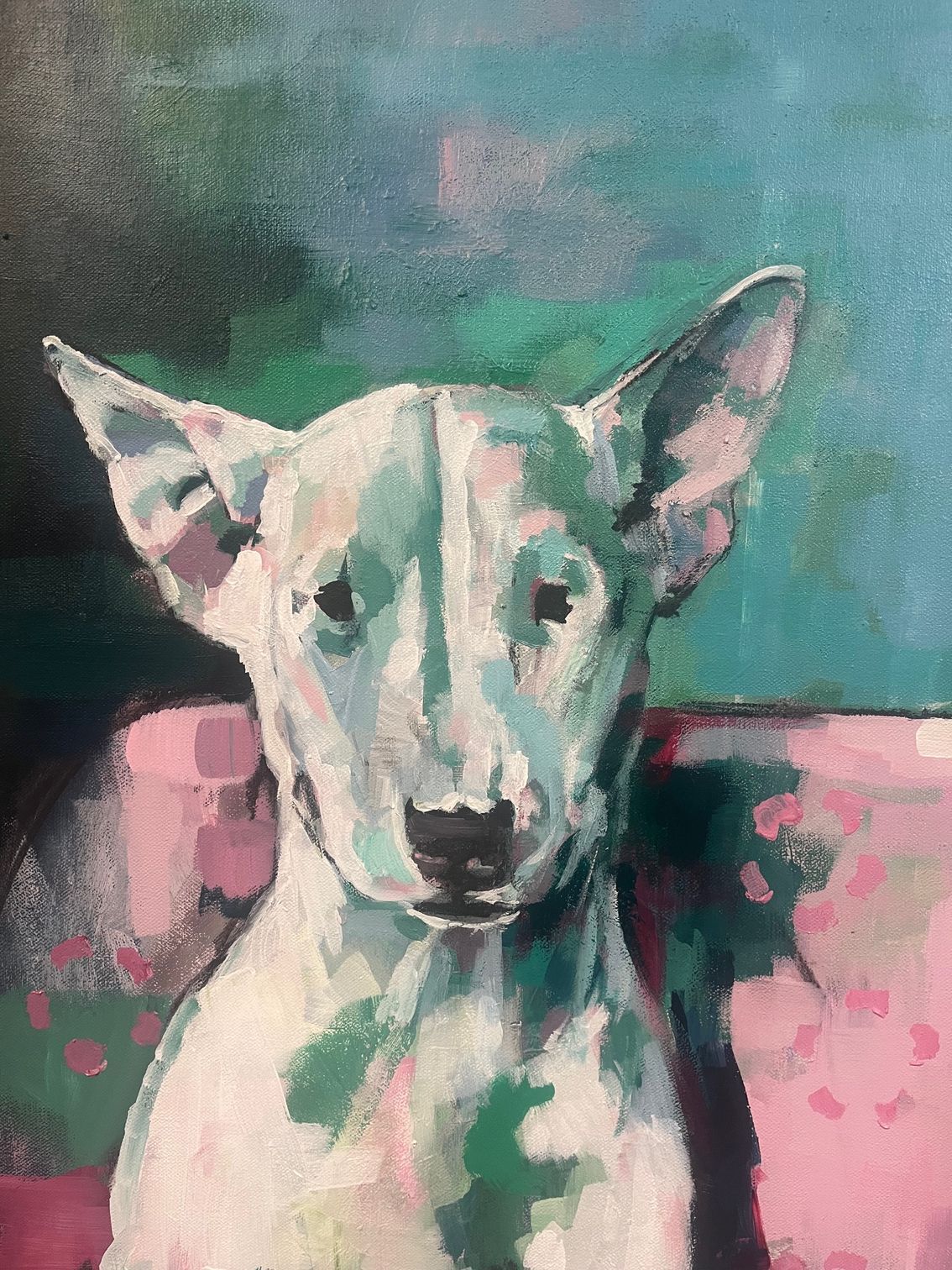 White dog with large ears sitting on a pink cushion against a teal background.