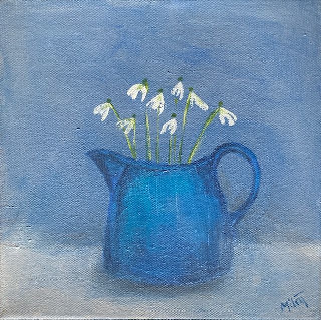Blue pitcher holding white snowdrop flowers against a blue background.