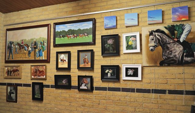 Gallery wall with diverse paintings, horses, and floral art on a brick wall.