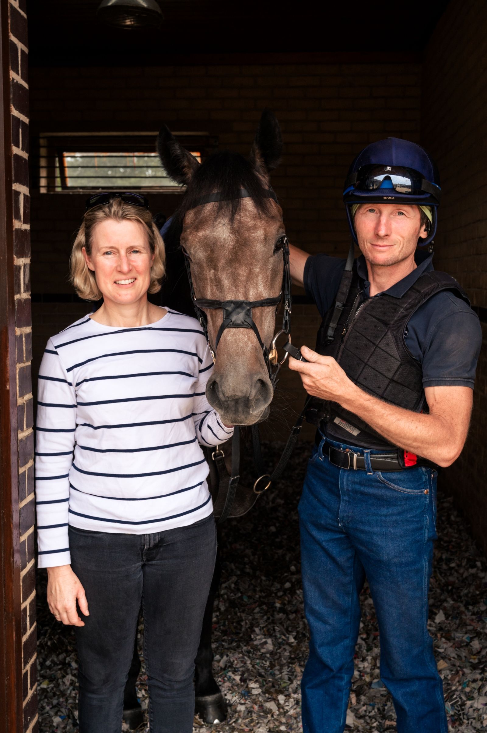 A man and a woman are standing next to a horse in a stable.