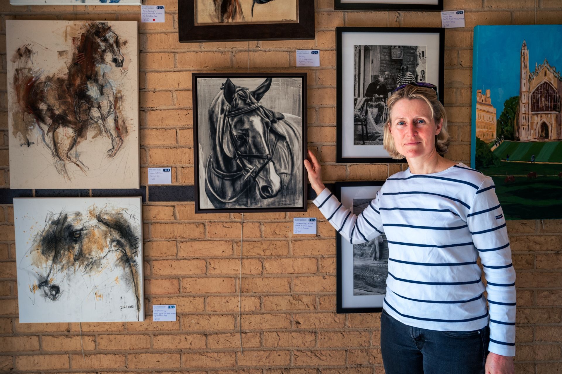 A woman is standing in front of a brick wall with paintings of horses on it.