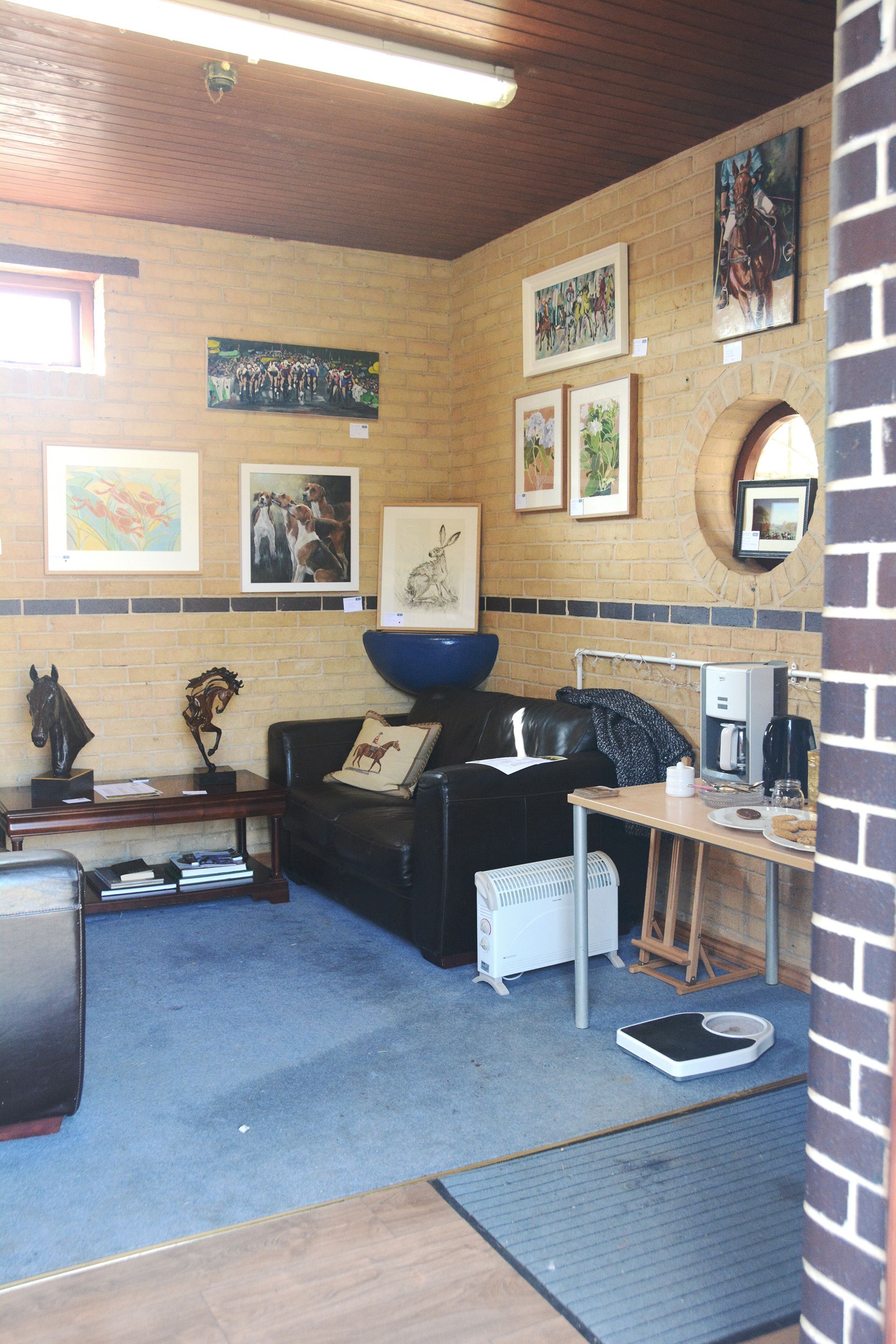 Small room with paintings on a brick wall. A couch, table, and coffee maker are present.