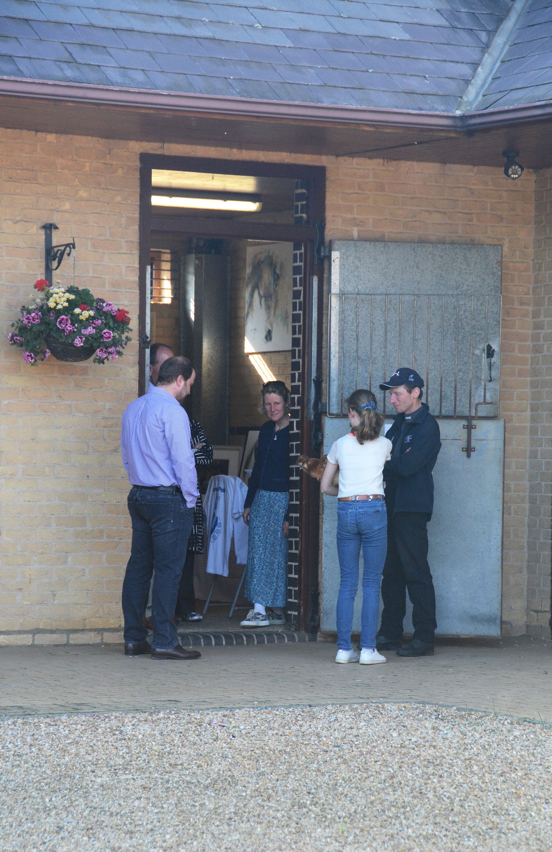 People stand near a stable door. One person wears a white shirt and blue jeans. Sunlight shines.