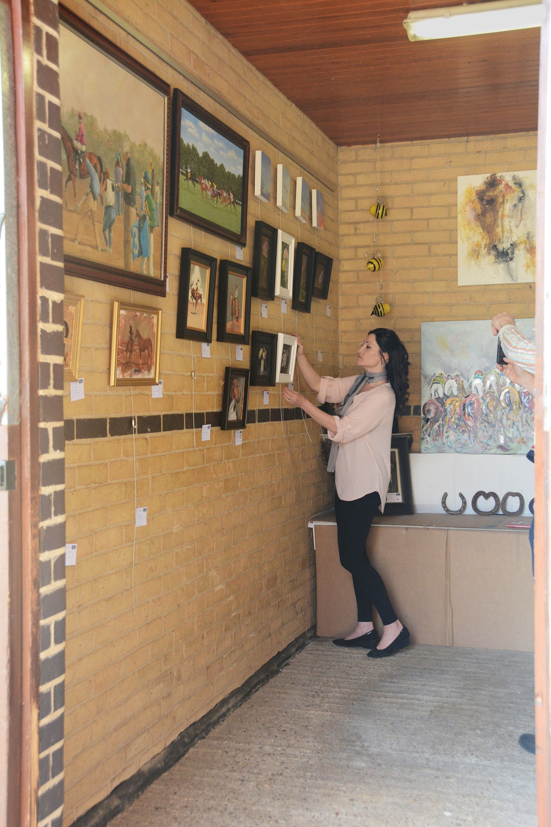 Woman arranging art in a gallery; brick wall, framed paintings.