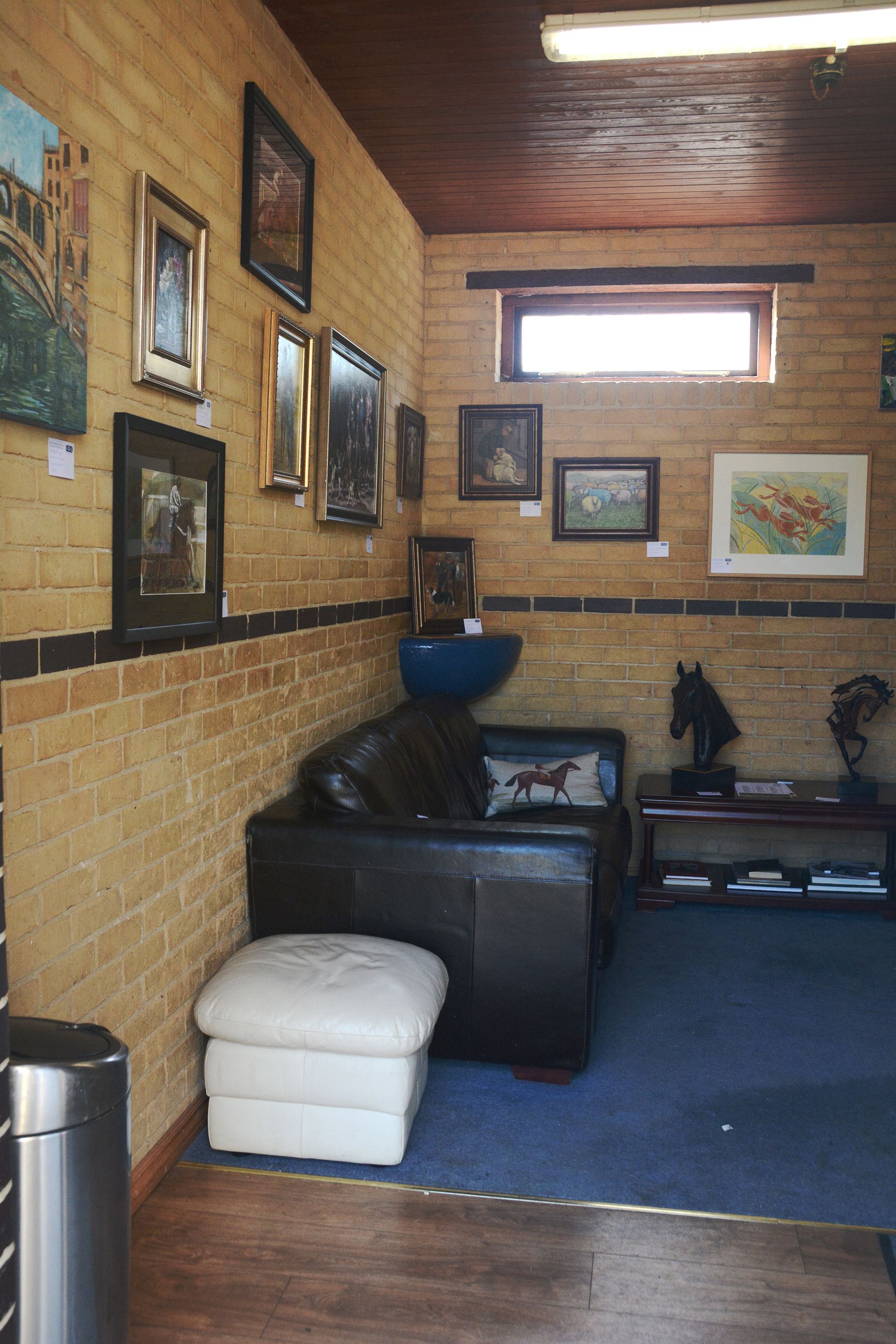 An art gallery interior with framed art on brick walls, a leather sofa, and a footrest.