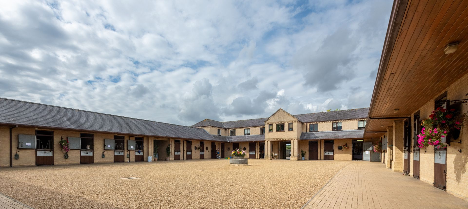 Courtyard of horse stables under a cloudy sky. Buildings are tan and brown.