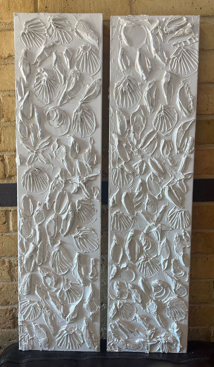 Two white paintings are sitting on a table in front of a brick wall.