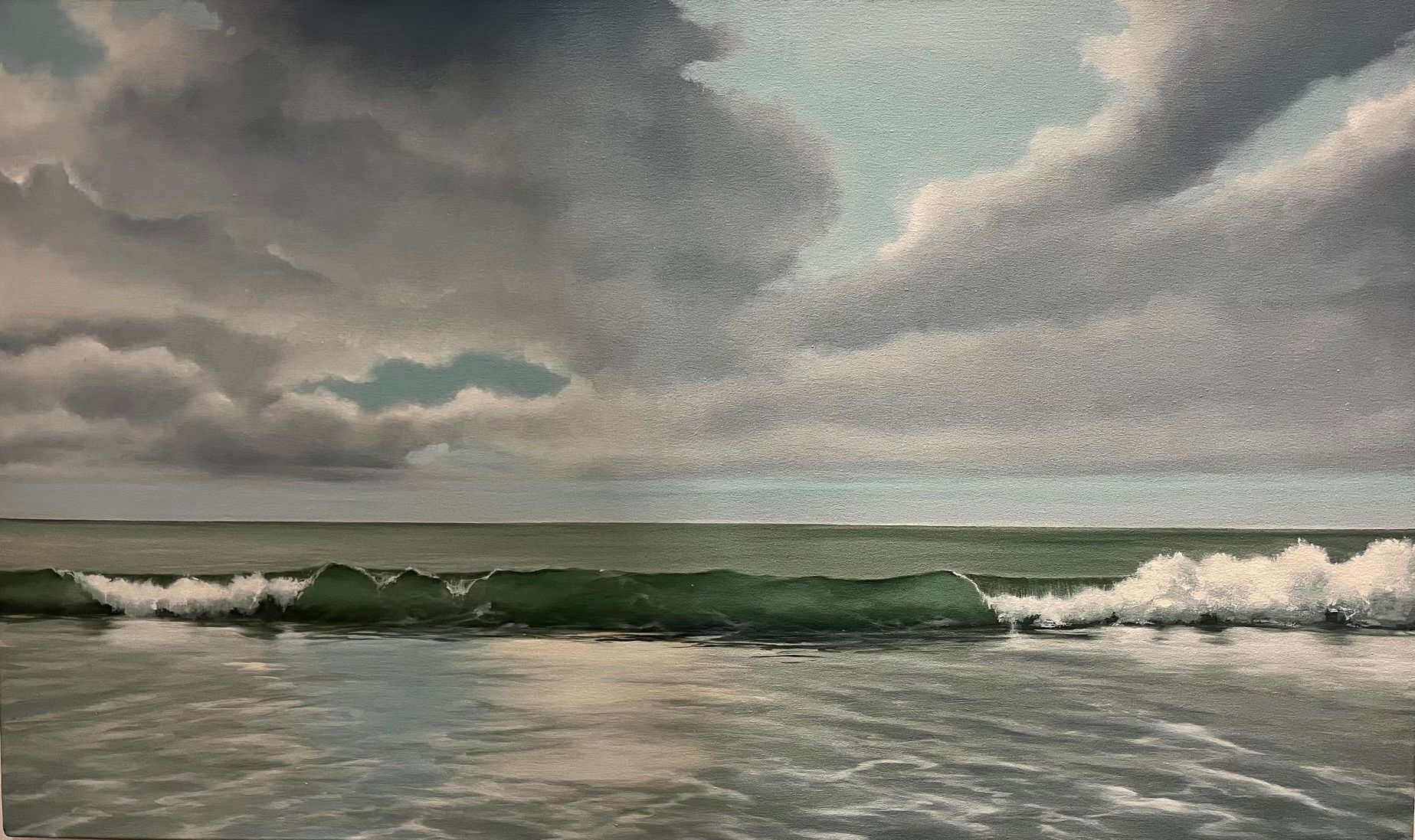 A wave crests toward a sandy shore beneath a dramatic, cloudy sky over a vast, calm ocean.