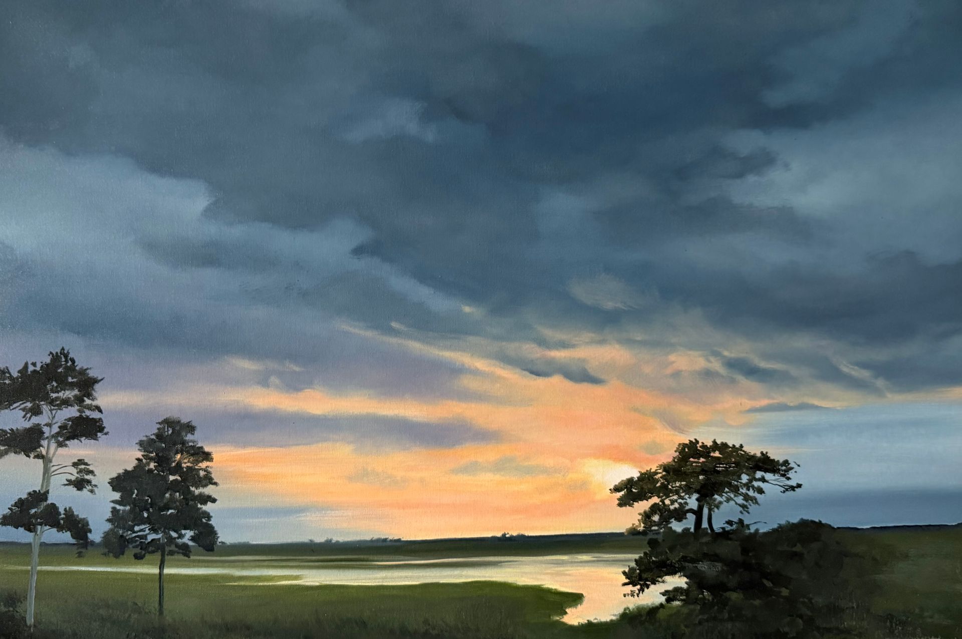 Stormy sunset over marsh with trees. Dark clouds, orange and yellow sky, water, and green marshland.