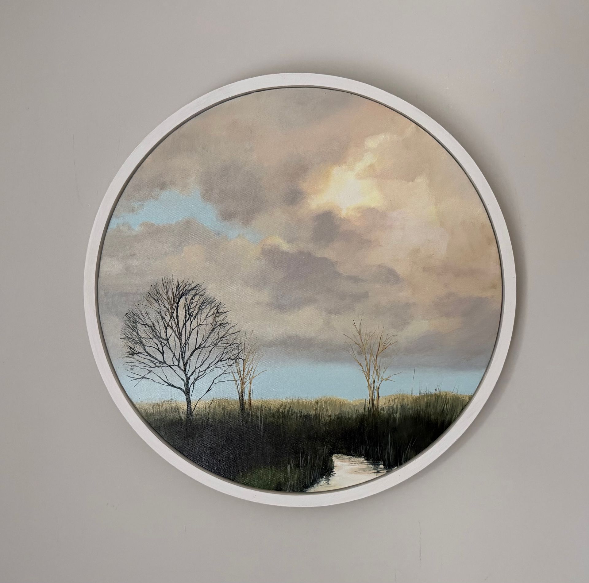Round painting of a landscape with trees and cloudy sky. Light illuminates clouds.
