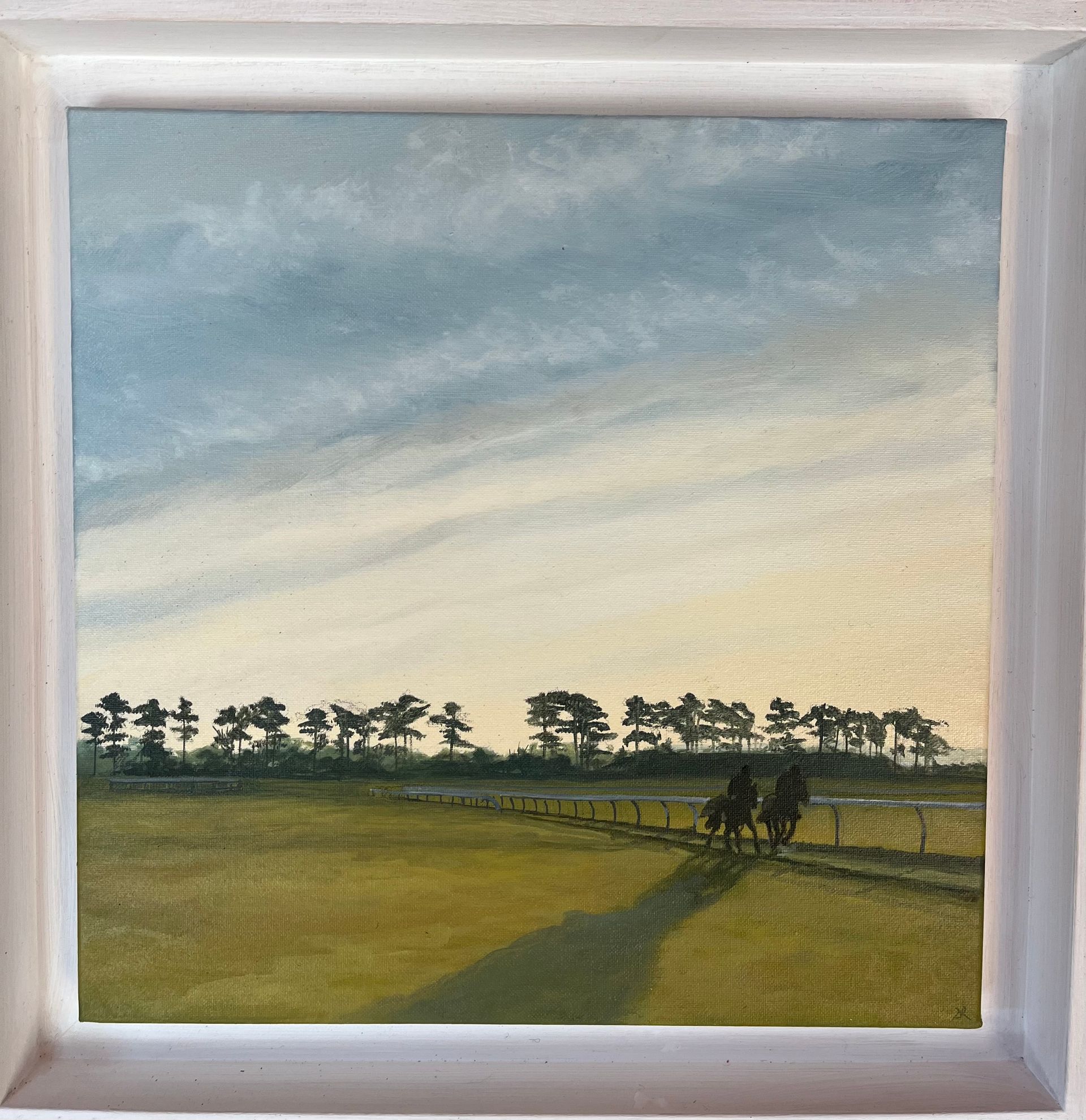 Two horses race on a track under a cloudy sky at sunset.