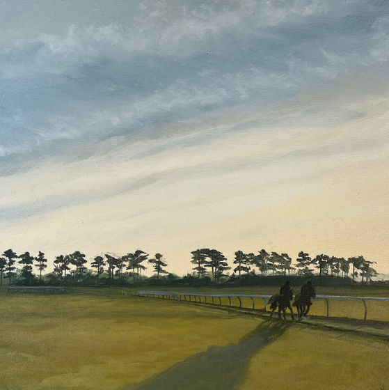 Two horses and riders on a race track at sunset, with trees on the horizon and a cloudy sky.