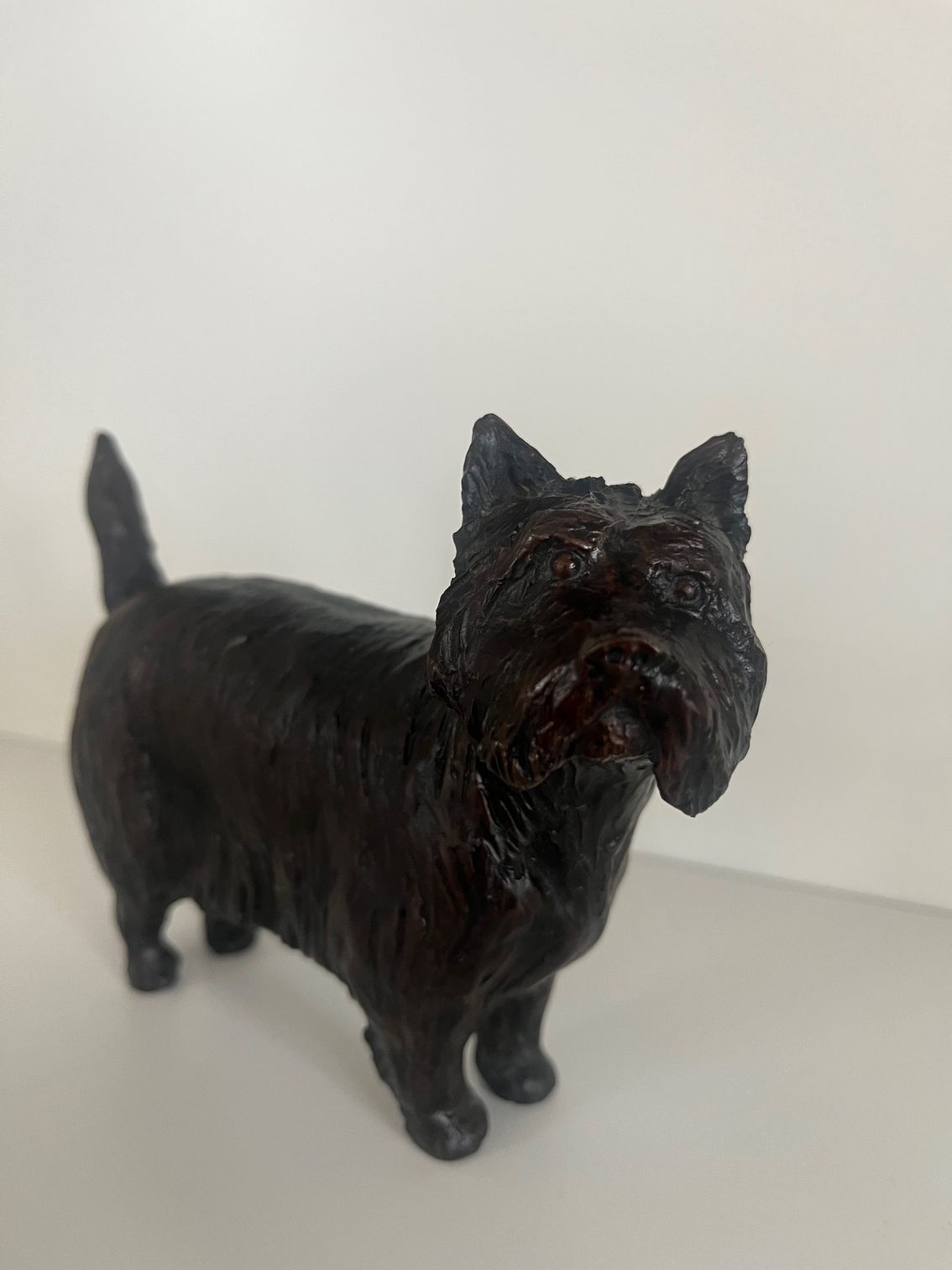 Dark-colored, small Scottish Terrier statue on a white surface.
