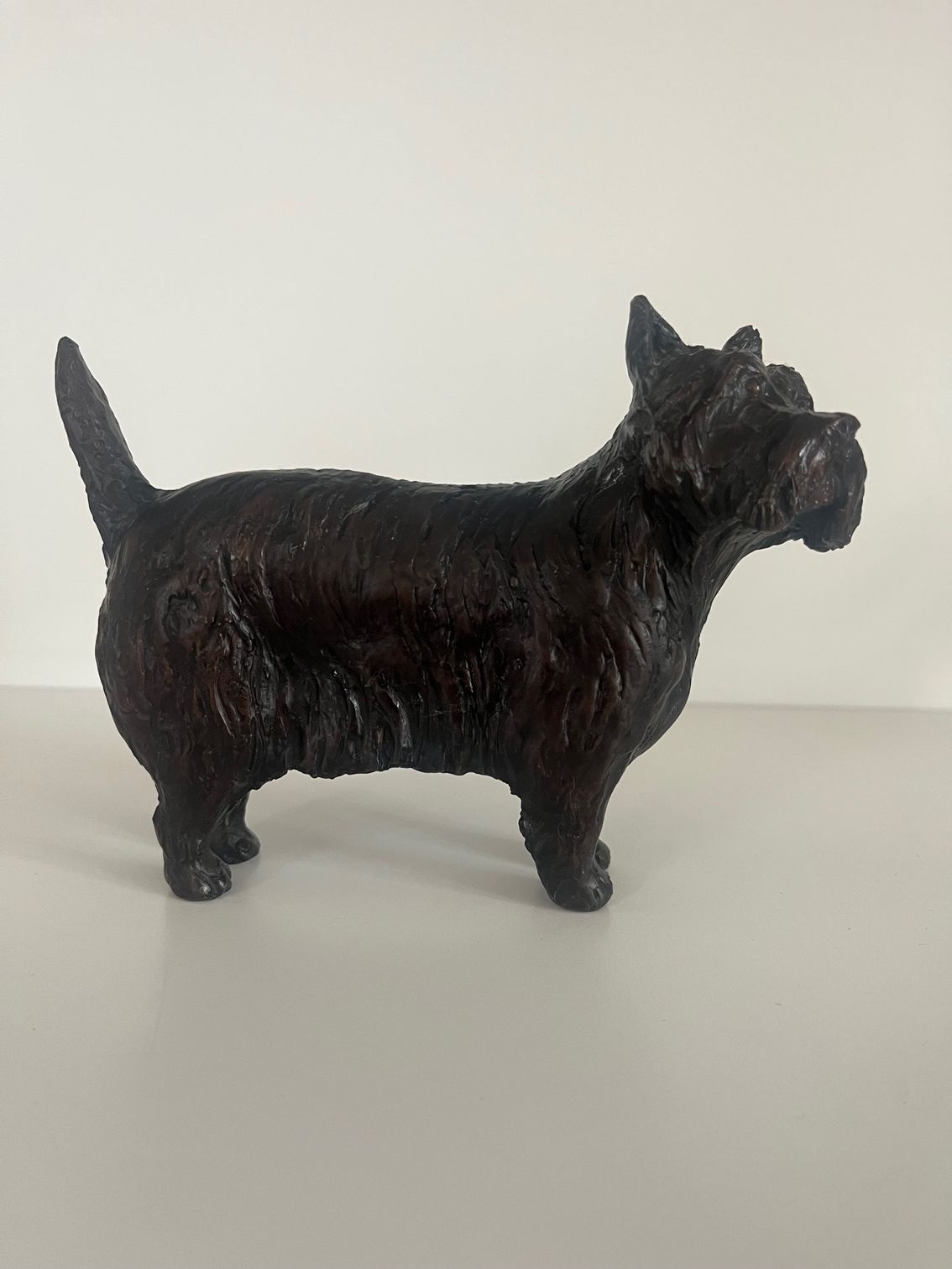 Bronze figurine of a Westie Terrier dog, standing on a white surface.