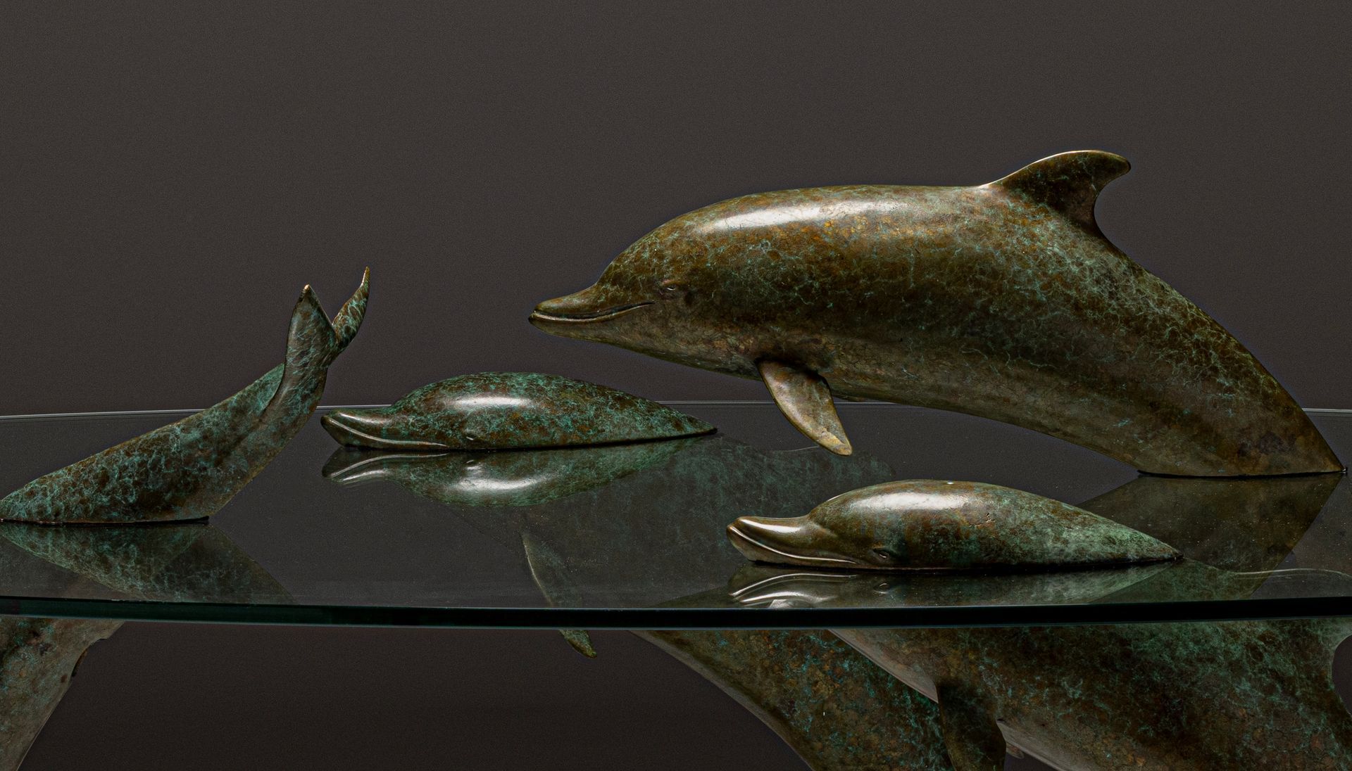 Glass-topped coffee table with dolphin sculptures as legs, bronze finish. Dolphins appear to be playing.