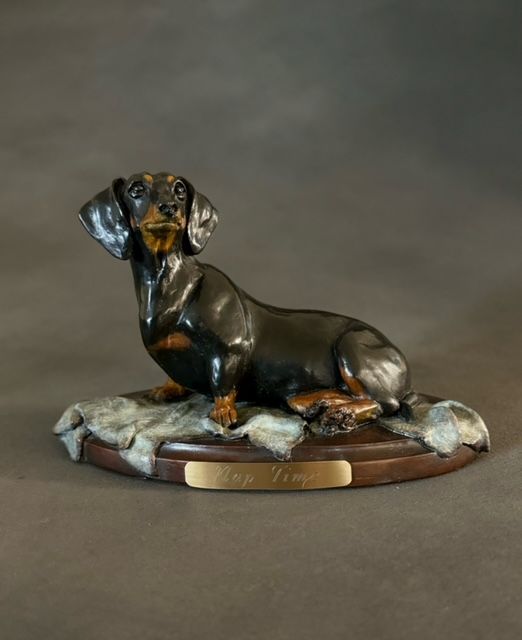Bronze Dachshund sculpture, black and tan, sitting on a wooden base.