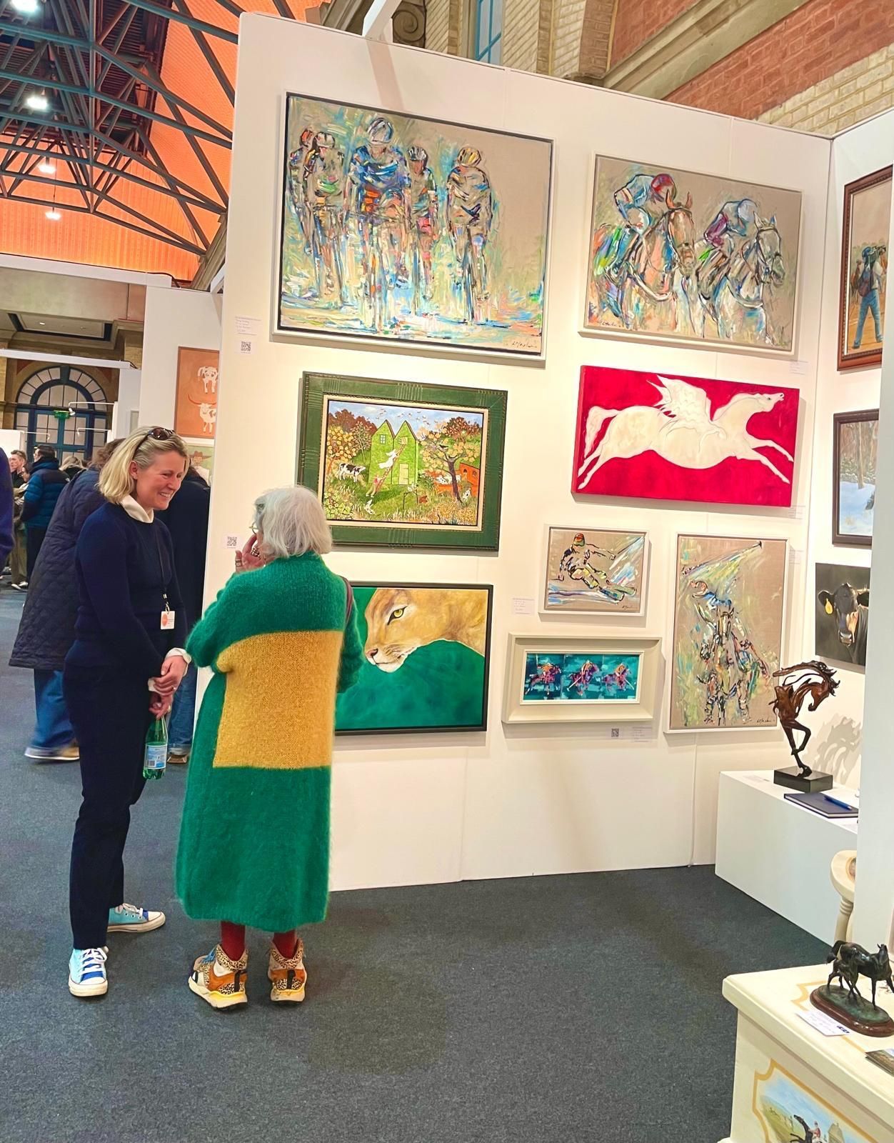 A woman in a green and yellow coat is looking at paintings on a wall