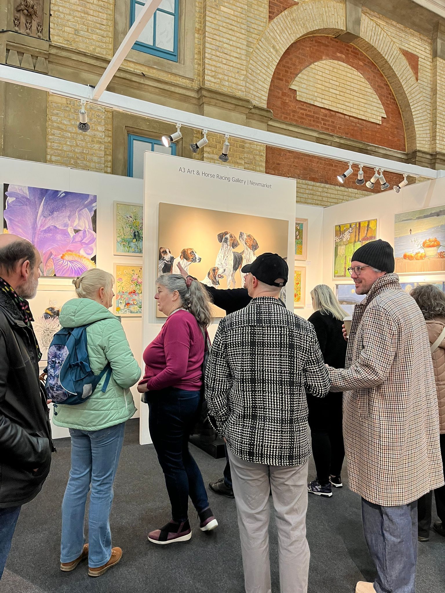 People viewing artwork at an art exhibition; colorful paintings displayed; interior setting.