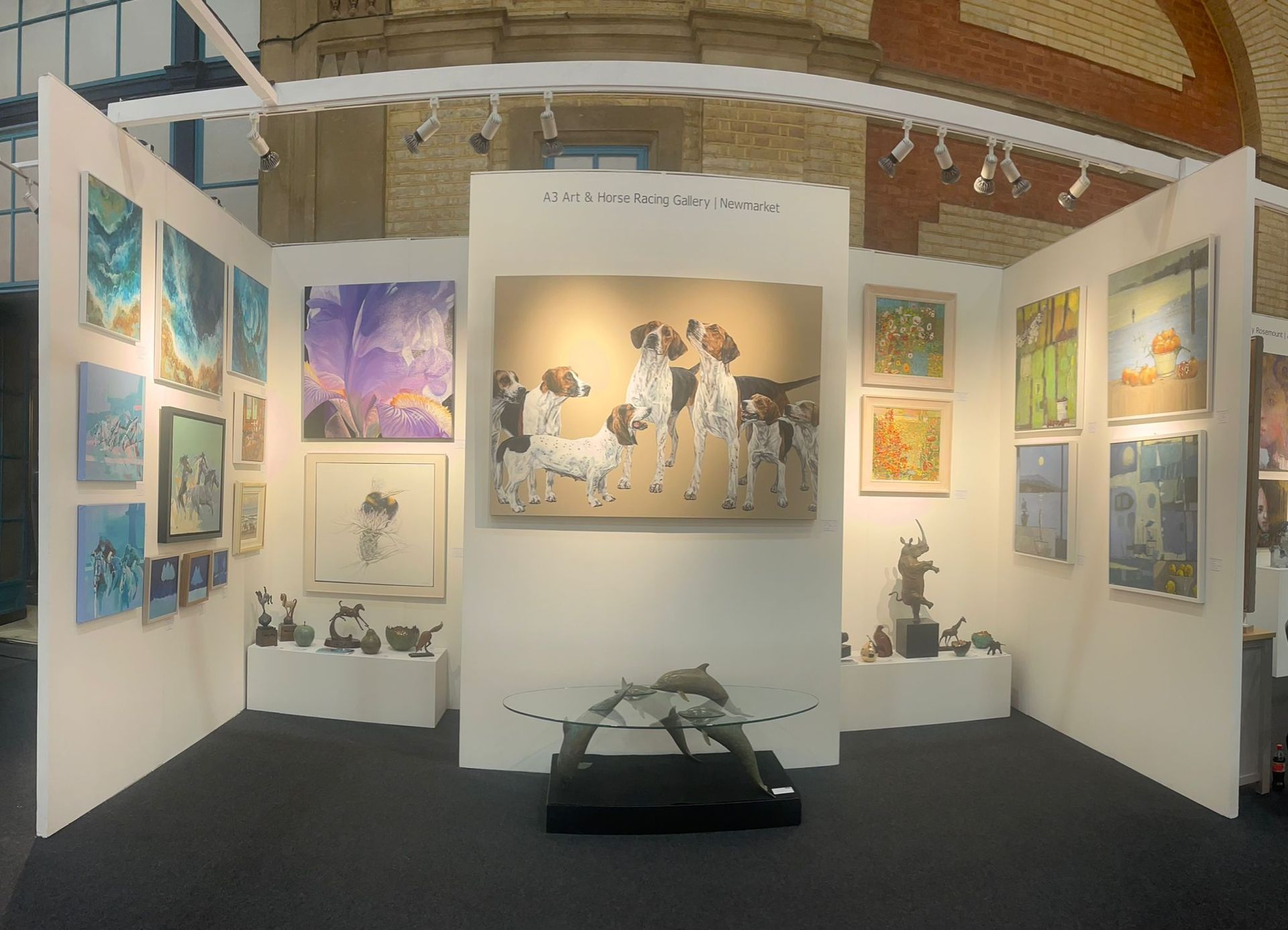 Art gallery booth featuring paintings and sculptures, with a central painting of dogs and a sculpture in front.