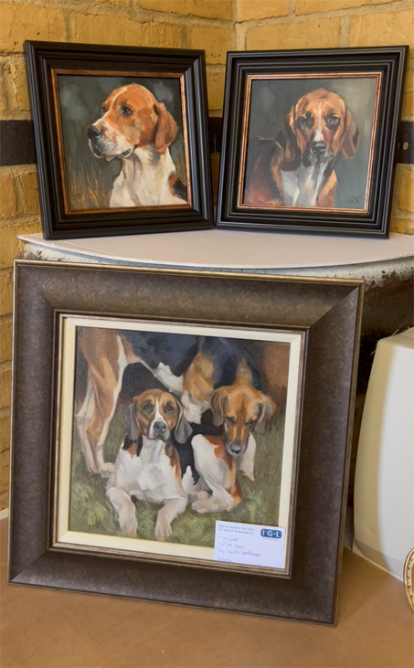 Three framed dog portraits, including one of a group of hounds, on a ledge against a brick wall.