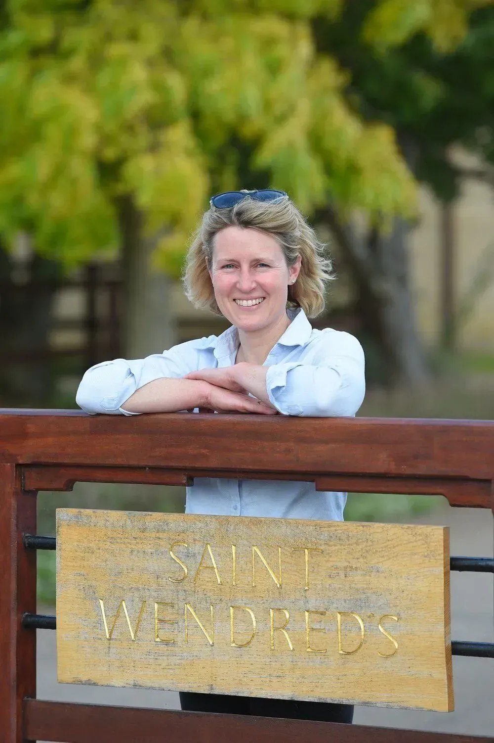 A woman is leaning on a wooden fence with a sign on it.