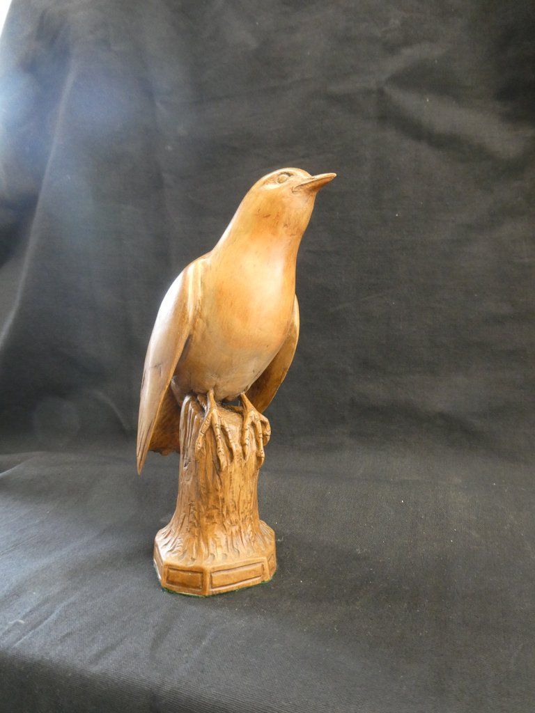 Carved wooden bird perched on a stump. Light brown color. Black background.