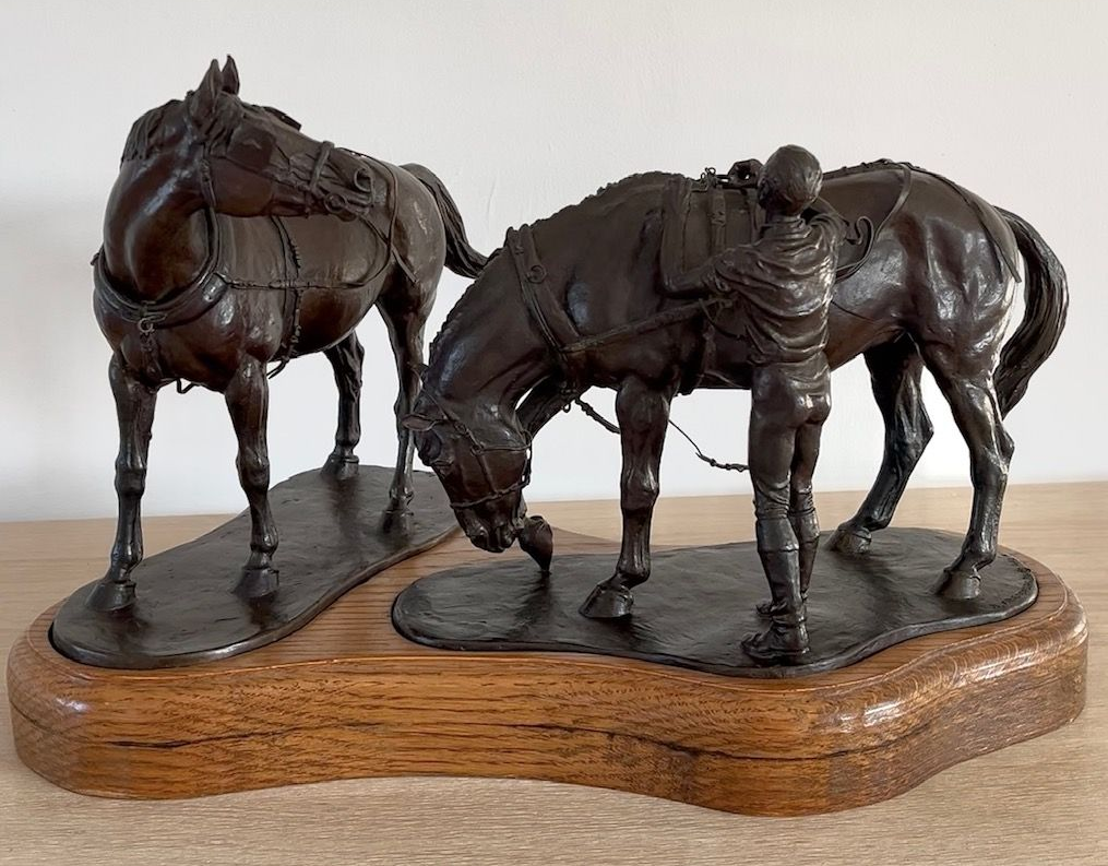 Bronze statue of two saddled horses, one grazing while a figure stands beside it.