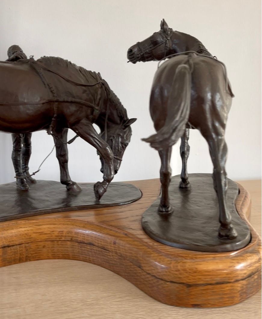 Bronze sculpture of two horses on a wooden base; one grazing, the other standing.