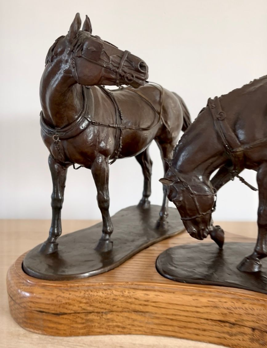 Bronze statue of two saddled horses, one grazing while a figure stands beside it.