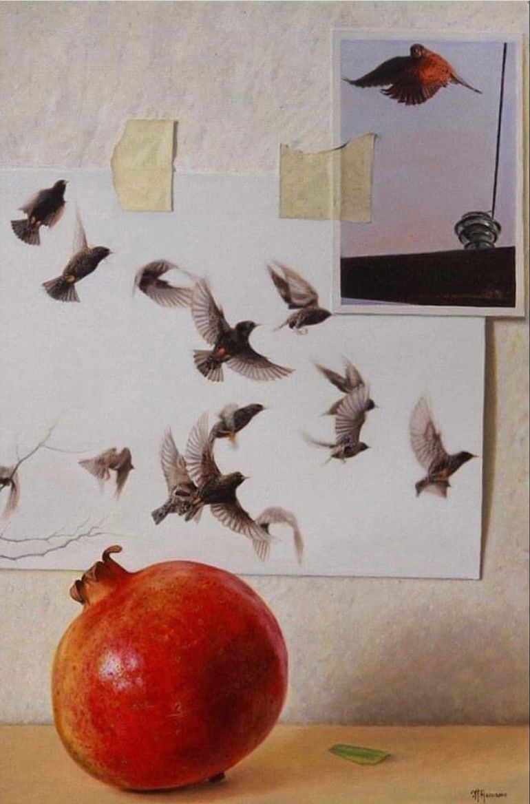 A pomegranate sits on a table in front of a painting of birds