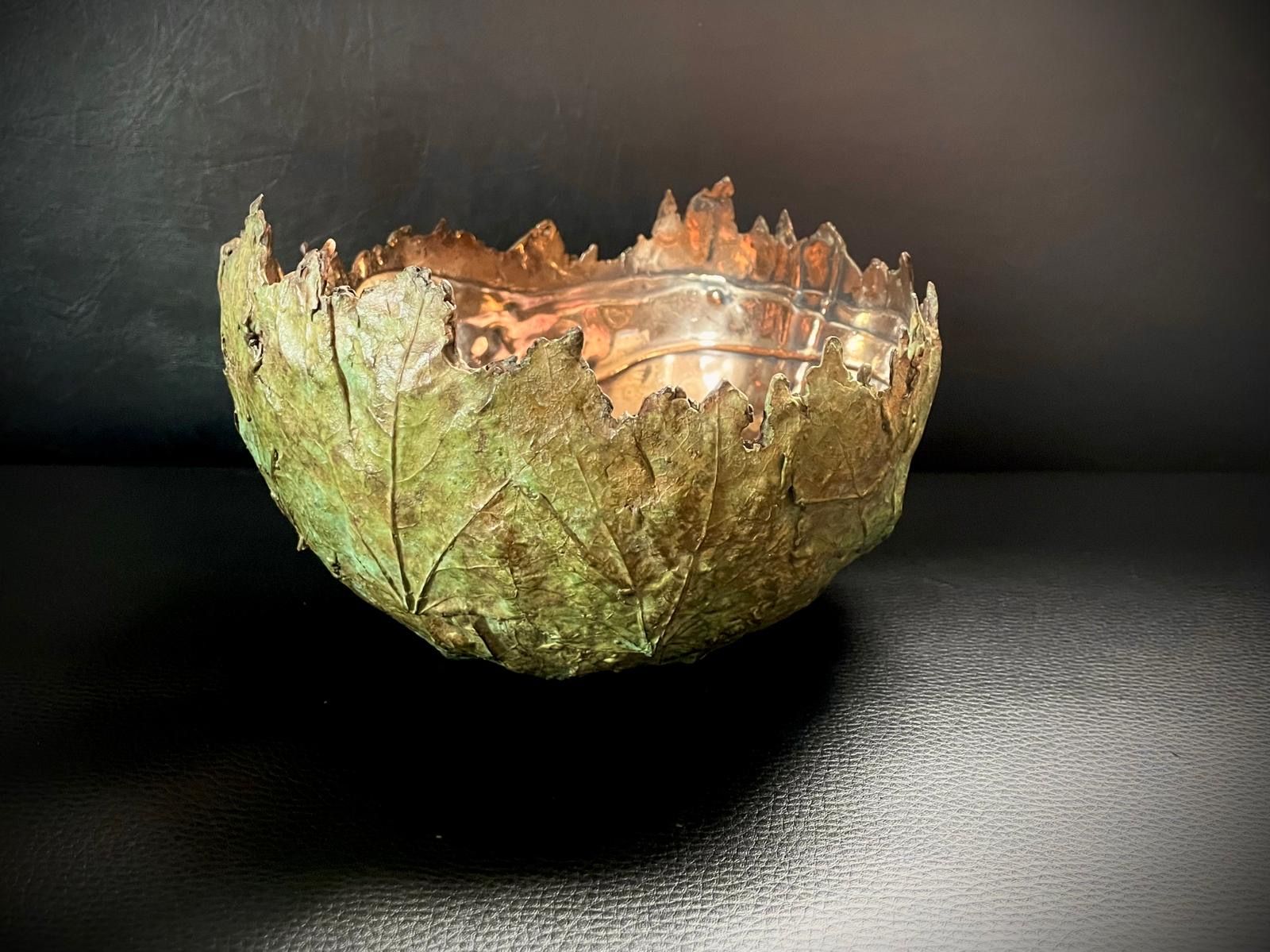 Copper bowl, exterior with green leafy texture, interior metallic, set on a dark surface.