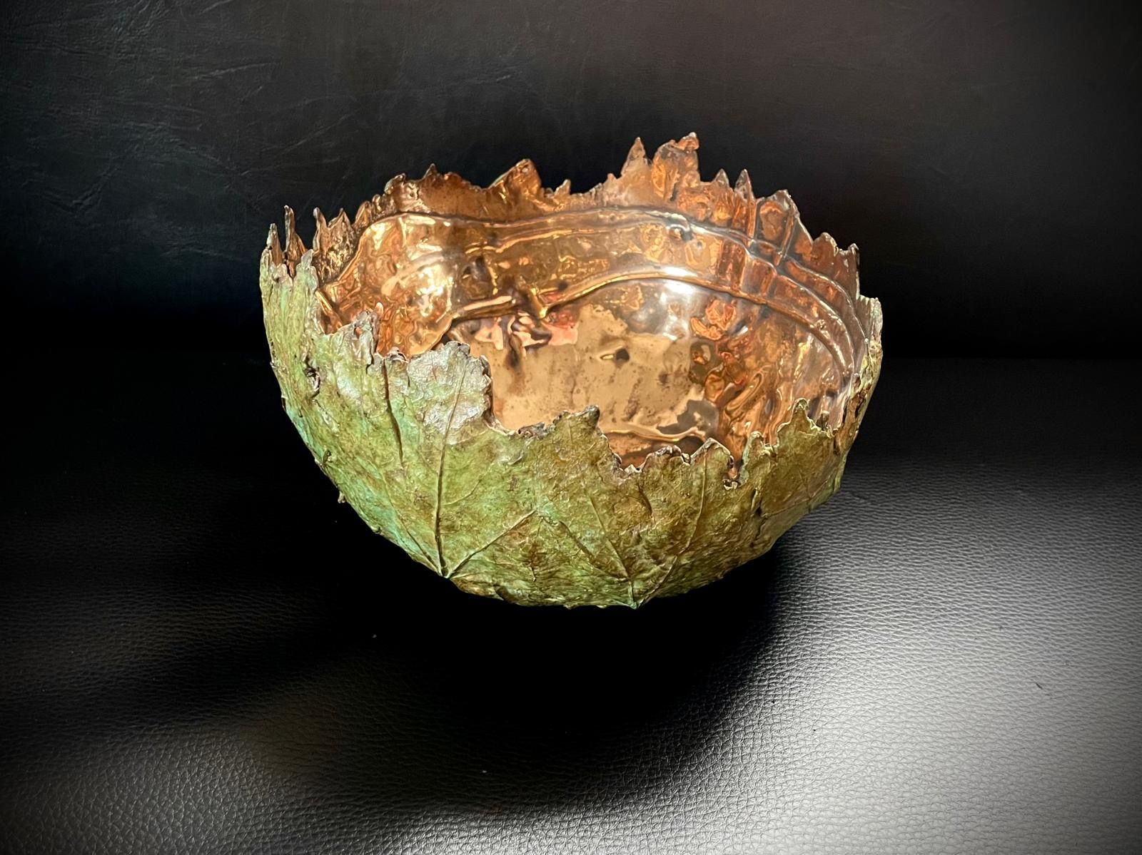 Copper bowl, exterior with green leafy texture, interior metallic, set on a dark surface.