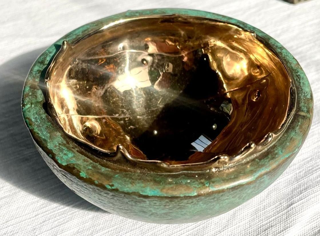 A green and gold bowl is sitting on a table.