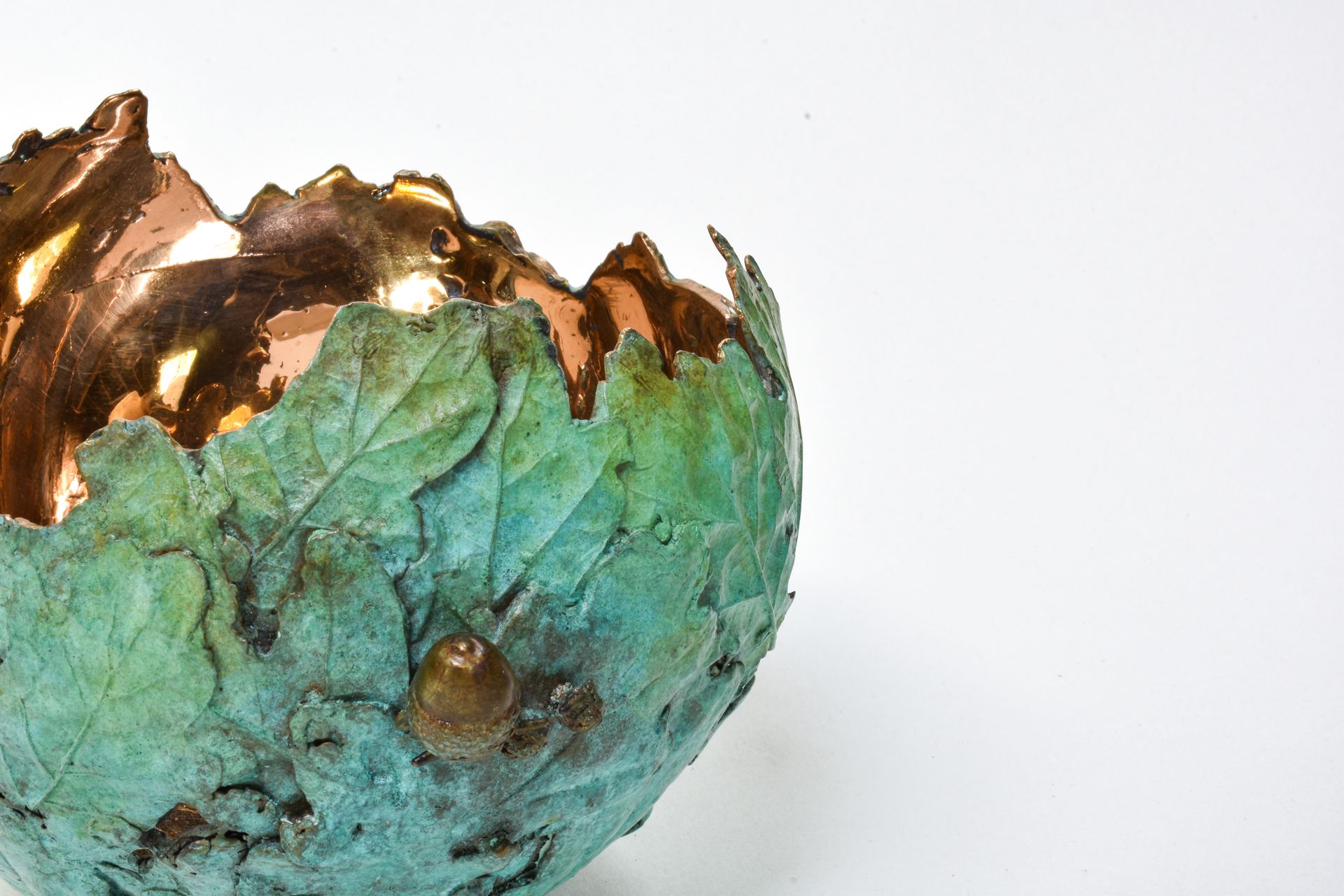 Copper bowl with leaf design, copper interior, blue-green patina on the exterior, and a light background.