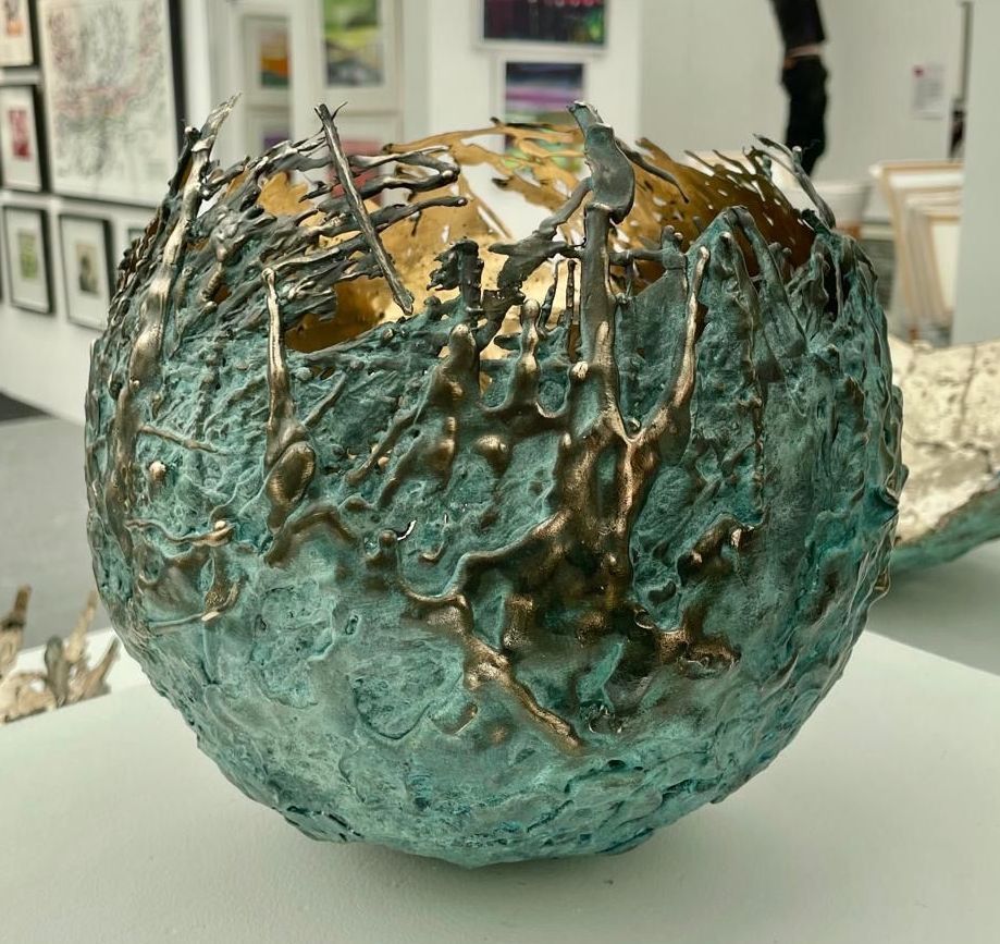 Sculpted bronze sphere with a textured teal exterior, gold interior, and ornate, dripped metal accents.