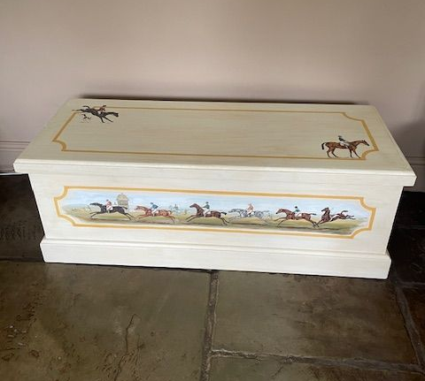 A white trunk with horses painted on it is sitting on a tiled floor.