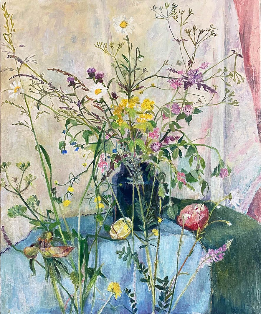 A bouquet of wildflowers in a blue vase on a blue tablecloth, against a light backdrop.